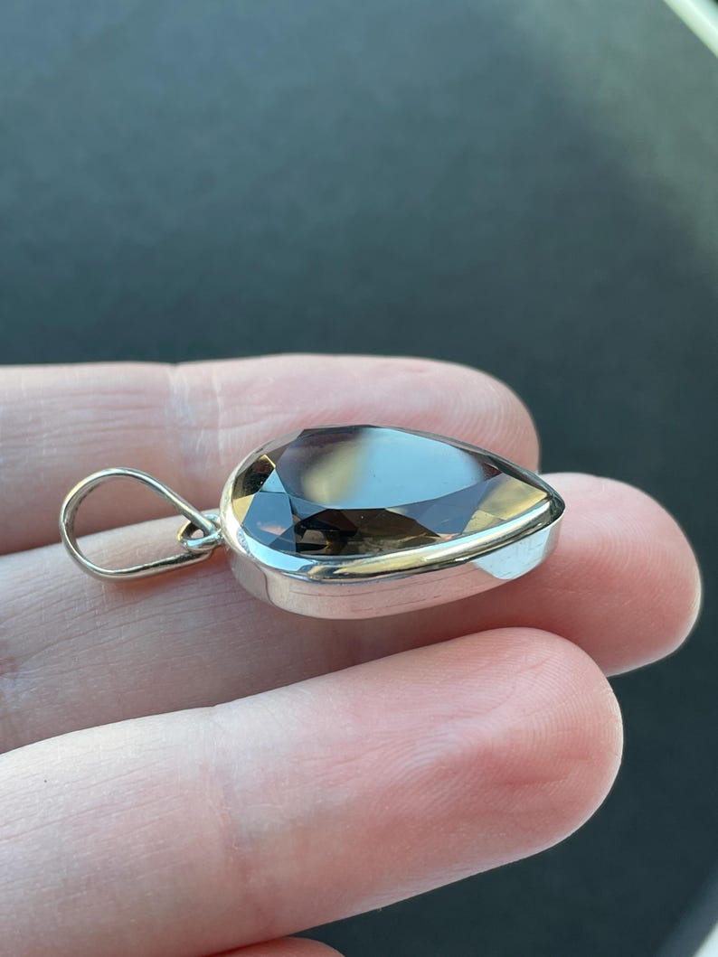May include: A silver pendant with a teardrop-shaped smoky quartz gemstone.
