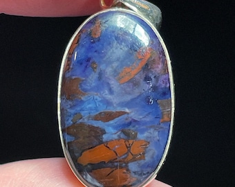 May include: A silver pendant featuring a blue and brown oval gemstone with a swirling pattern. The pendant is set in a silver frame.