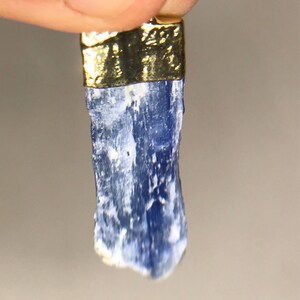 May include: A blue kyanite crystal pendant with a gold-plated setting. The crystal is raw and has a natural, rough texture.