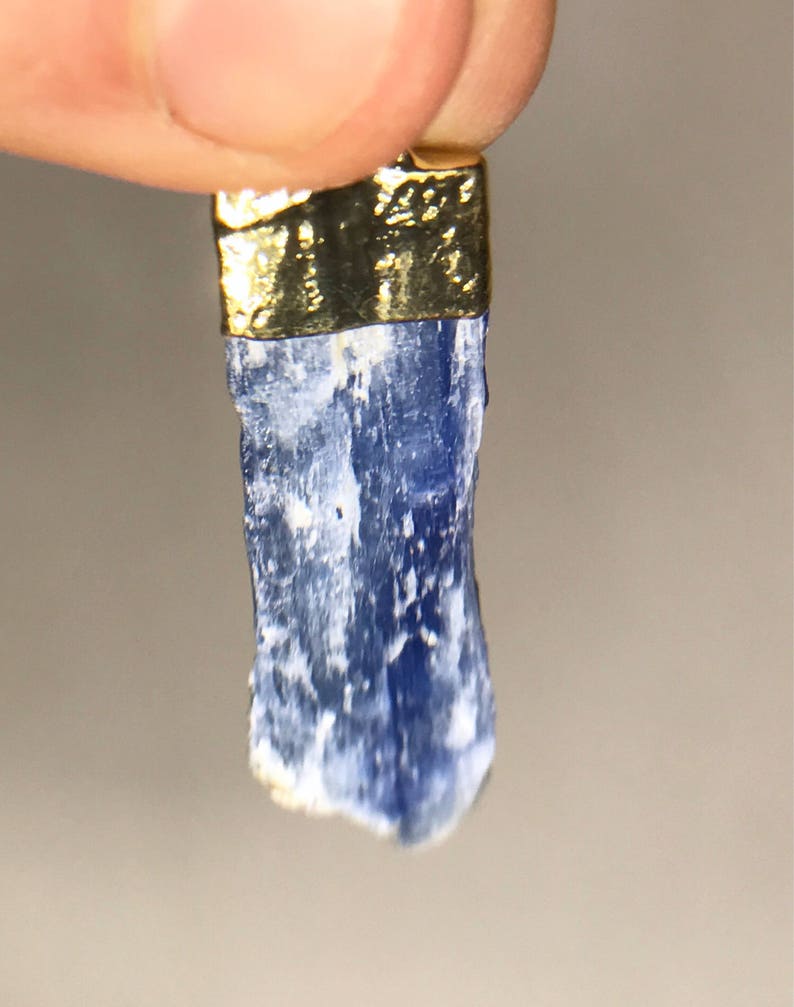 May include: A blue kyanite crystal pendant with a gold-plated setting. The crystal is raw and has a natural, rough texture.