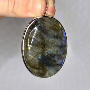 May include: A silver oval pendant with a large, iridescent labradorite gemstone. The stone has a dark gray base with flashes of blue, green, and gold.