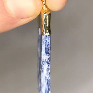 May include: A blue kyanite pendant with a gold-plated bail. The pendant is a long, thin rectangle with a pointed end.