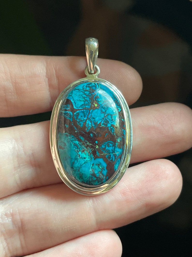 Peut inclure: Un pendentif en argent avec une grande pierre turquoise de forme ovale. La pierre pr&eacute;sente un motif tourbillonnant de bleu, de vert et de brun.