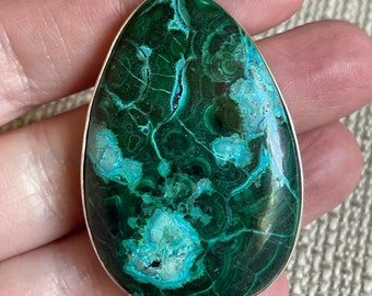 May include: A green and blue malachite gemstone pendant with a silver bail. The pendant is oval shaped and has a swirling pattern.