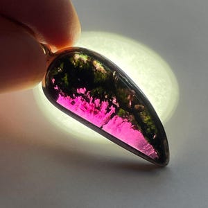 May include: A pendant featuring a green and pink gemstone with a silver setting. The gemstone has a unique, layered pattern.