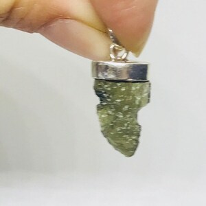 May include: A silver pendant featuring a raw, green, and sparkly, teardrop-shaped stone.