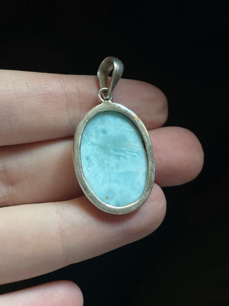 Puede incluir: Un colgante de plata con una piedra ovalada de color azul claro. El colgante tiene un dise&ntilde;o sencillo y es perfecto para a&ntilde;adir un toque de elegancia a cualquier atuendo.