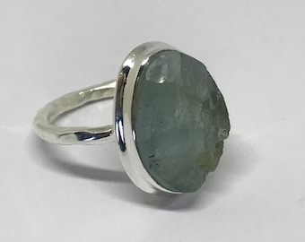 Könnte beinhalten: Ein silberner Ring mit einem großen, hellblauen Aquamarin, der in einer Zargenfassung gefasst ist. Der Ringarm ist gehämmert und hat eine strukturierte Oberfläche.