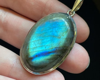May include: A silver pendant featuring a large oval-shaped labradorite gemstone with iridescent blue and green hues.