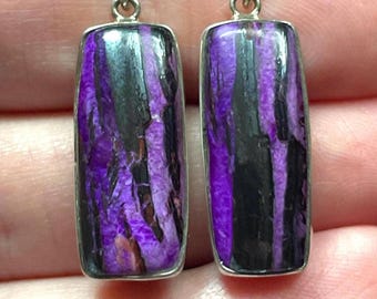 May include: A pair of rectangular earrings with a silver-colored frame. The earrings feature a striking pattern of purple and black streaks, creating a unique and eye-catching design. The earrings are suspended from a small silver loop.