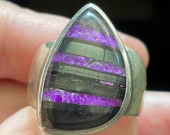 May include: A silver ring with a teardrop-shaped purple and black gemstone. The gemstone has a layered pattern of purple and black.