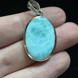 Puede incluir: Un colgante de plata con una piedra ovalada de color azul claro. La piedra tiene un patr&oacute;n de remolino y nublado.