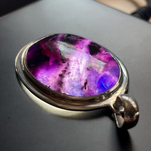 May include: A silver pendant with a large oval-shaped purple and white gemstone. The gemstone has a swirling pattern and is set in a silver bezel.