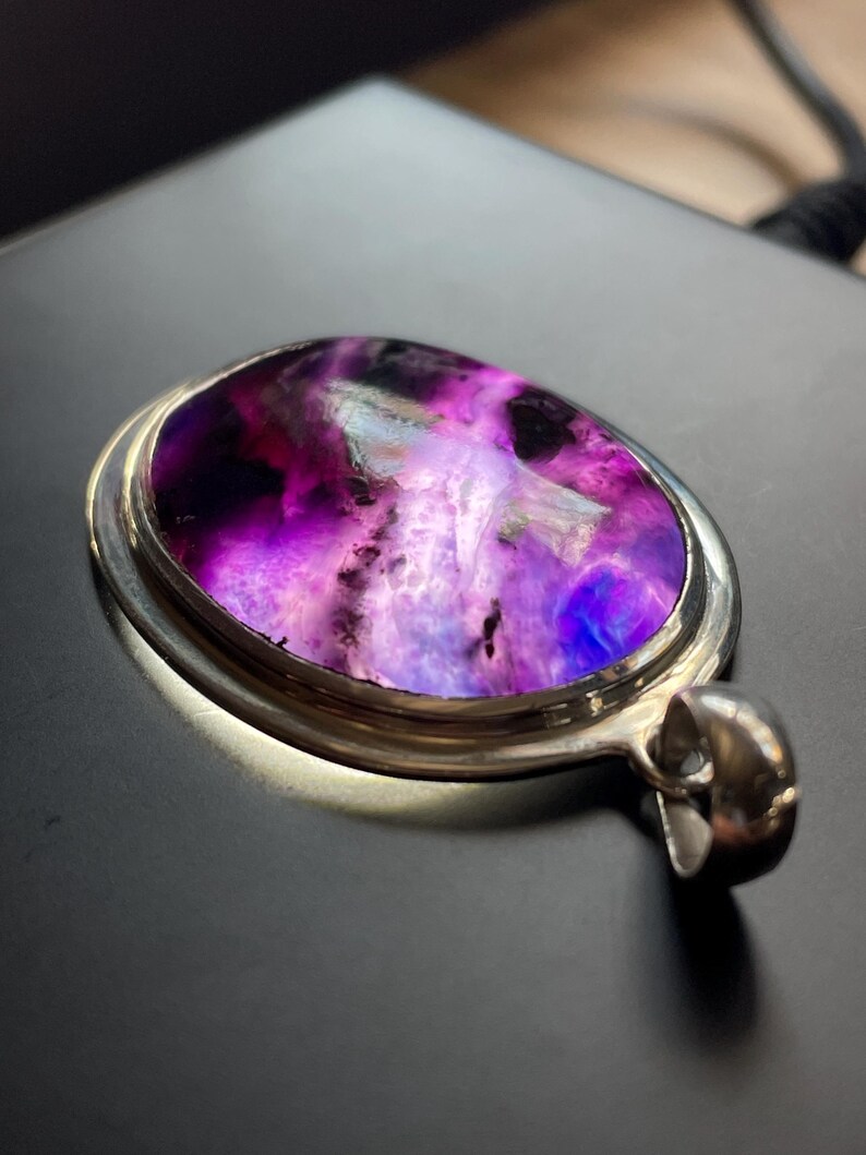 May include: A silver pendant with a large oval-shaped purple and white gemstone. The gemstone has a swirling pattern and is set in a silver bezel.