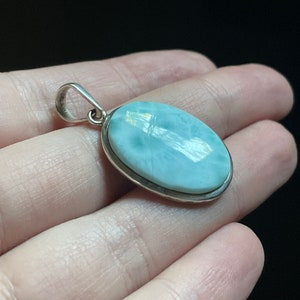 Puede incluir: Un colgante de plata con una piedra ovalada de color azul claro. La piedra tiene un aspecto nublado y veteado.