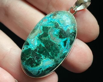 May include: A silver pendant featuring a large oval-shaped green and blue gemstone with a swirling pattern. The gemstone is set in a silver bezel.