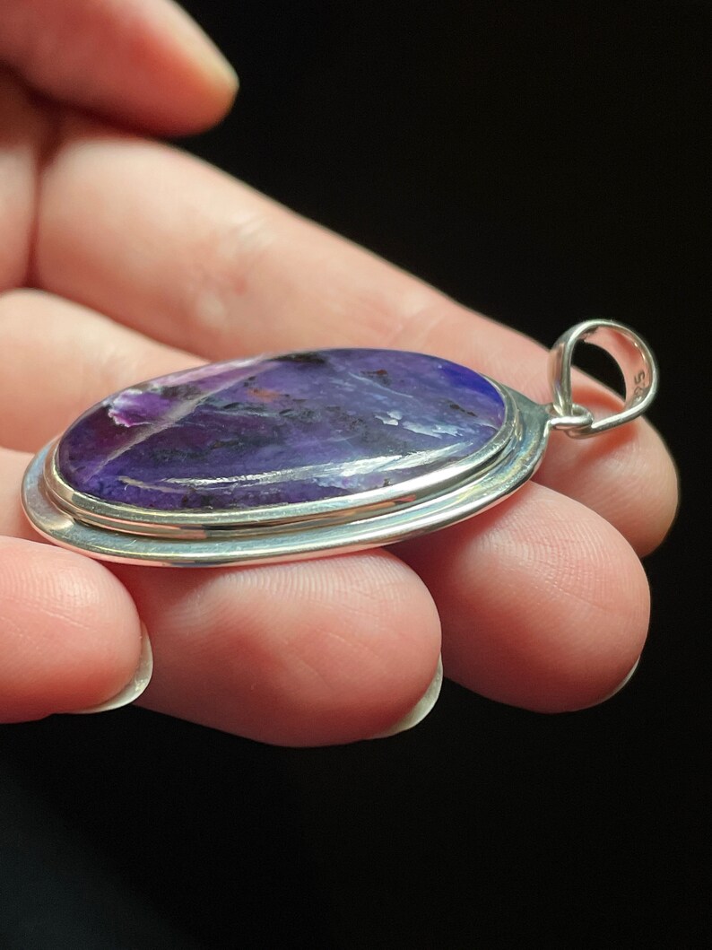 May include: A silver pendant with a purple and white oval gemstone. The pendant has a silver bail.