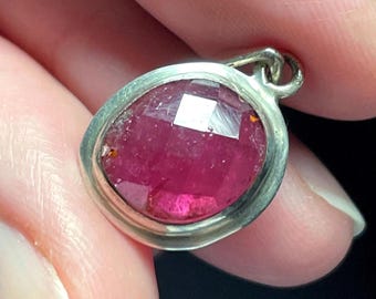 May include: A silver pendant featuring a faceted pink gemstone set in a bezel setting.