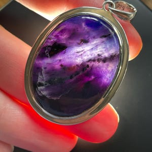 May include: A silver pendant with a large oval-shaped purple and white stone. The pendant is marked "925" on the bail.