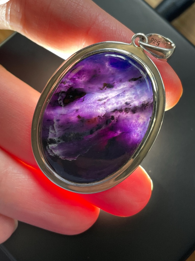 May include: A silver pendant with a large oval-shaped purple and white stone. The pendant is marked "925" on the bail.