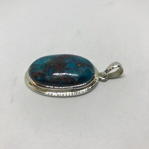 Peut inclure: Un pendentif en argent avec une pierre ovale bleue et brune sertie dans une b&eacute;li&egrave;re en argent.