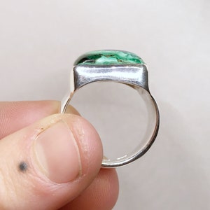 K&ouml;nnte beinhalten: Ein Silberring mit einem polierten, rechteckigen, gr&uuml;n-schwarz gemusterten Edelstein, der in einer glatten Metallfassung sitzt. Die Ringschiene ist breit und aus reflektierendem, silberfarbenem Metall gefertigt, mit einer soliden Oberfl&auml;che.