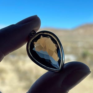 May include: A teardrop-shaped pendant with a clear, faceted gemstone set in a silver-toned metal setting.