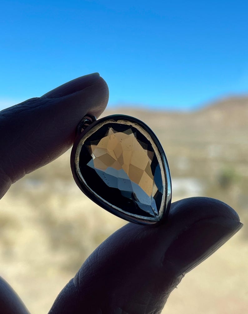 May include: A teardrop-shaped pendant with a clear, faceted gemstone set in a silver-toned metal setting.