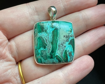 May include: A silver pendant featuring a green and white malachite stone with a swirling pattern. The stone is set in a silver frame and has a rectangular shape.