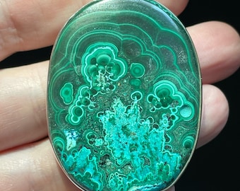 May include: A silver pendant featuring a large oval-shaped malachite stone with a green and white swirling pattern.