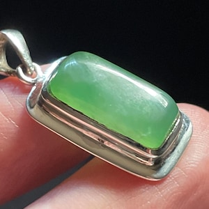 May include: A silver pendant featuring a rectangular green jade stone set in a double-rimmed bezel.