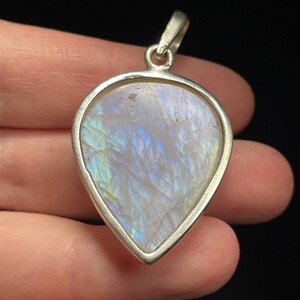 May include: A teardrop-shaped pendant with a white iridescent gemstone set in a silver frame.