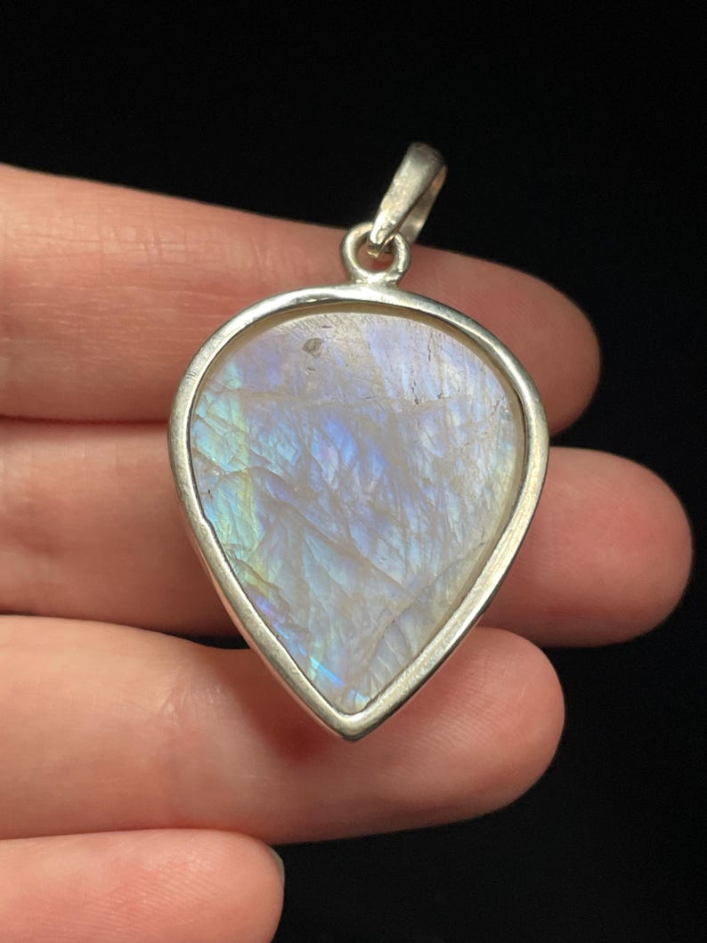 May include: A teardrop-shaped pendant with a white iridescent gemstone set in a silver frame.