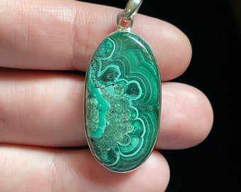 May include: A silver pendant featuring a green malachite stone with a swirling pattern. The stone is oval-shaped and set in a silver bezel.