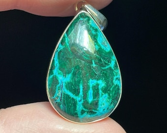 May include: A teardrop-shaped pendant with a vibrant green and blue malachite stone set in a silver-colored metal frame. The stone's surface displays intricate patterns and textures, creating a unique and eye-catching piece of jewelry.