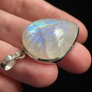 May include: A silver pendant with a large, iridescent moonstone. The stone is set in a silver bezel and has a teardrop shape.