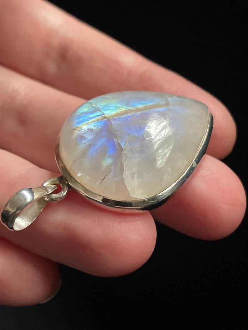 May include: A silver pendant with a large, iridescent moonstone. The stone is set in a silver bezel and has a teardrop shape.