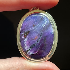May include: A silver pendant with a purple and white oval gemstone. The gemstone has a swirling pattern and a shiny finish.