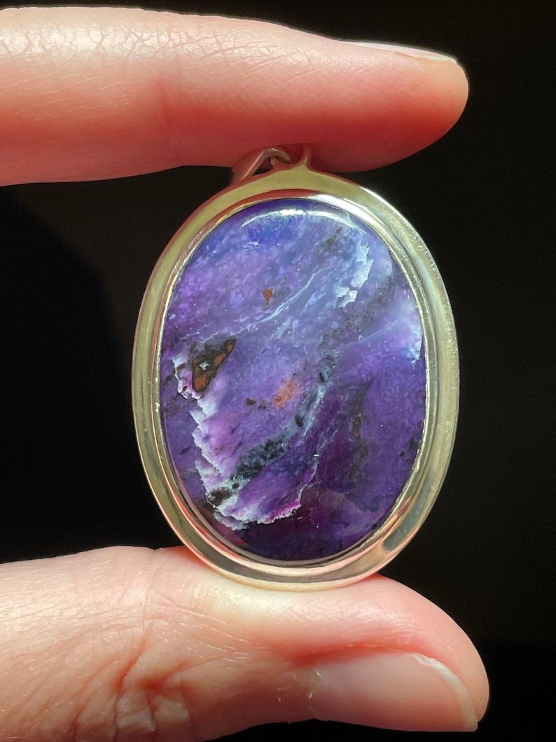 May include: A silver pendant with a purple and white oval gemstone. The gemstone has a swirling pattern and a shiny finish.
