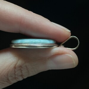 Puede incluir: Un colgante de plata con una piedra preciosa azul claro engastada en un bisel de plata. El colgante tiene una simple anilla para sujetarlo a una cadena.