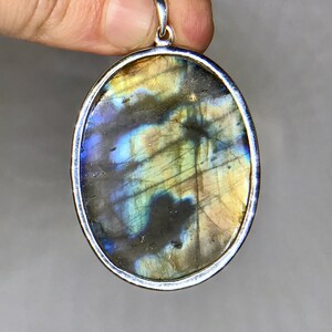 May include: A silver oval pendant with a large, iridescent labradorite gemstone. The stone has a mix of blue, green, and gold colors.