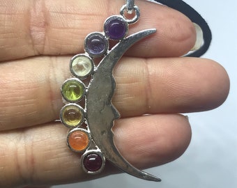 May include: A silver crescent moon pendant with seven round gemstones in a rainbow of colors. The stones are amethyst, clear quartz, green aventurine, yellow citrine, orange carnelian, red garnet, and purple amethyst.