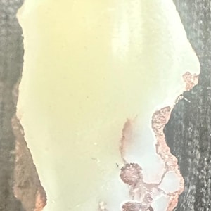 May include: A pale yellow, irregularly shaped stone with a rough, textured edge. The stone has areas of reddish-brown and white coloration, creating a unique, natural appearance. The stone is likely a decorative or collectible item.