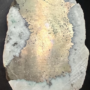 May include: A natural stone specimen with a metallic gold-colored center and a white and gray outer edge. The stone has a rough, irregular shape and a textured surface. The gold section has dark speckles and a slight iridescence. The stone is likely a mineral specimen.