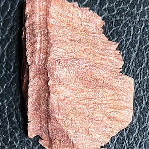 May include: A close-up of a piece of copper foil with a textured surface. The foil is a warm, reddish-brown color with a slight iridescent sheen.