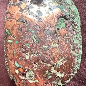 May include: A rough, irregularly shaped rock with a mix of copper and green hues. The surface shows areas of oxidation, with patches of bright copper and green, and hints of other colors.