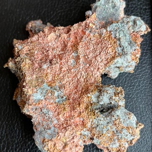 May include: A close-up of a rough, irregular shaped piece of copper ore with a reddish-brown color and white and gold flecks.