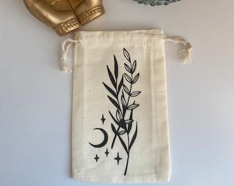 May include: A small white cotton drawstring bag with a black and white design of a crescent moon, stars, and stylized leaves.