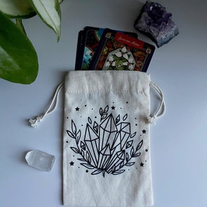 May include: A white cotton drawstring bag with a black and white illustration of crystals and leaves. The bag has a star pattern and the text "Spirit and Matter" is visible on a card inside the bag.
