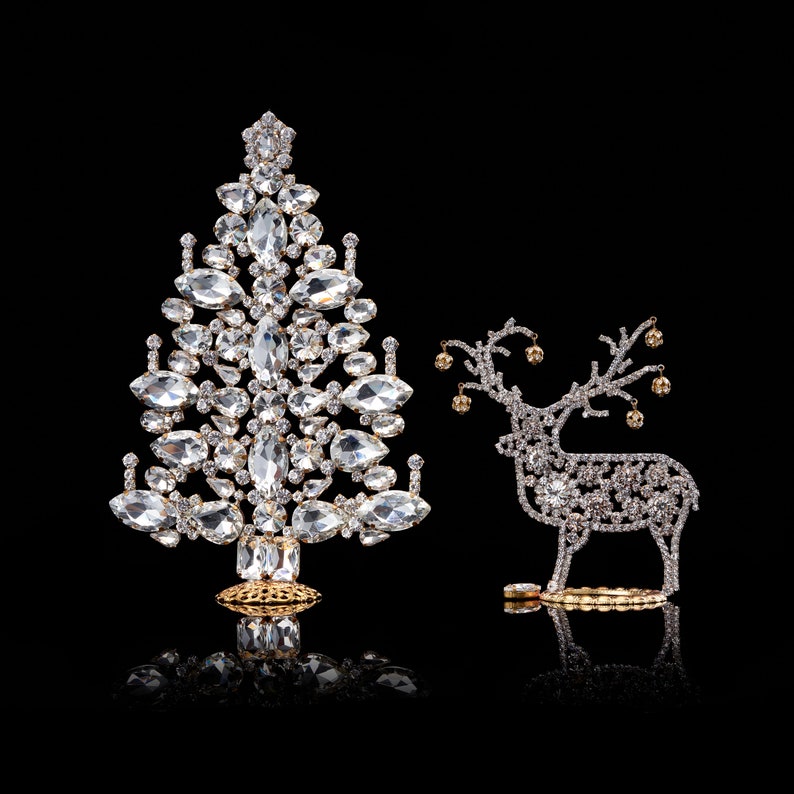 May include: A sparkling silver reindeer and a crystal Christmas tree ornament, both decorated with rhinestones, on a black background.